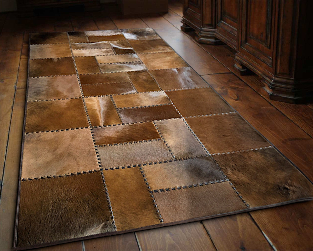 A rectangular patchwork leather rug featuring a mosaic of stitched brown and tan leather panels in various textures and tones, shown against a plain white background.