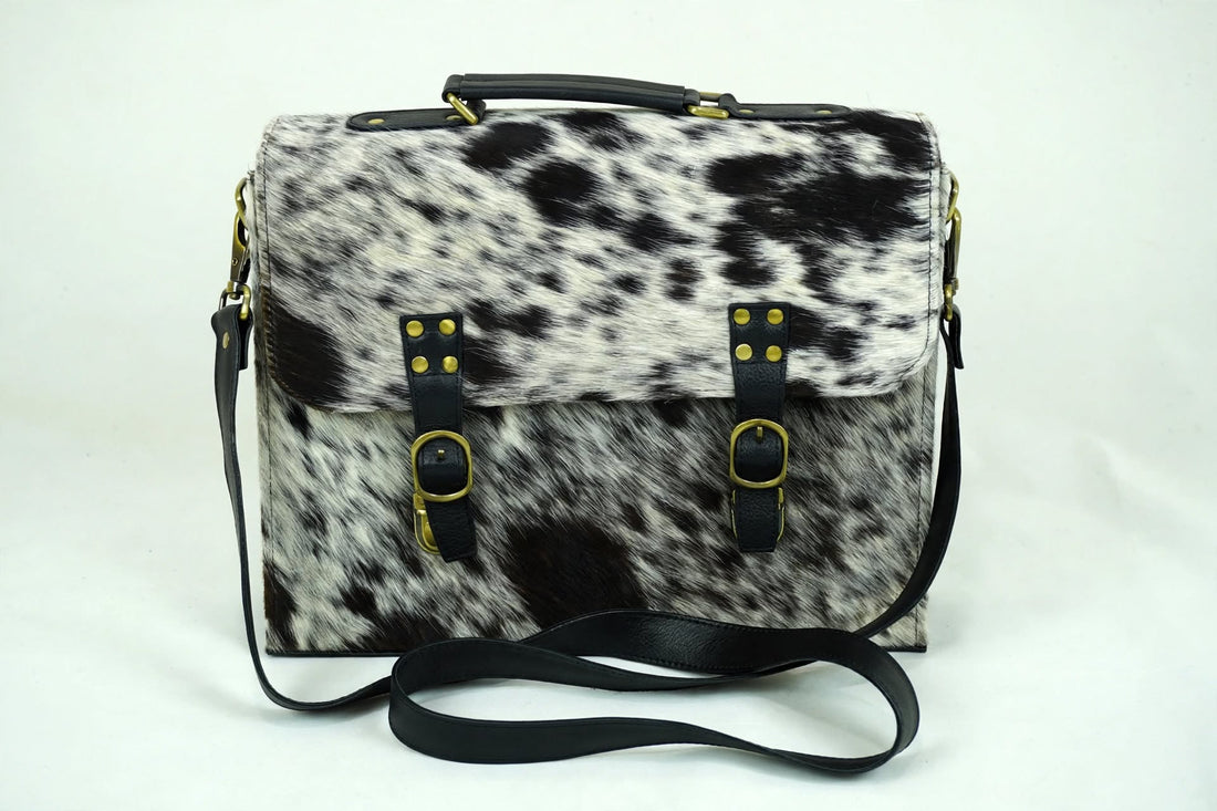 Salt and pepper spotted cowhide messenger bag with black leather trim and brass buckle straps - front view hero shot on white background