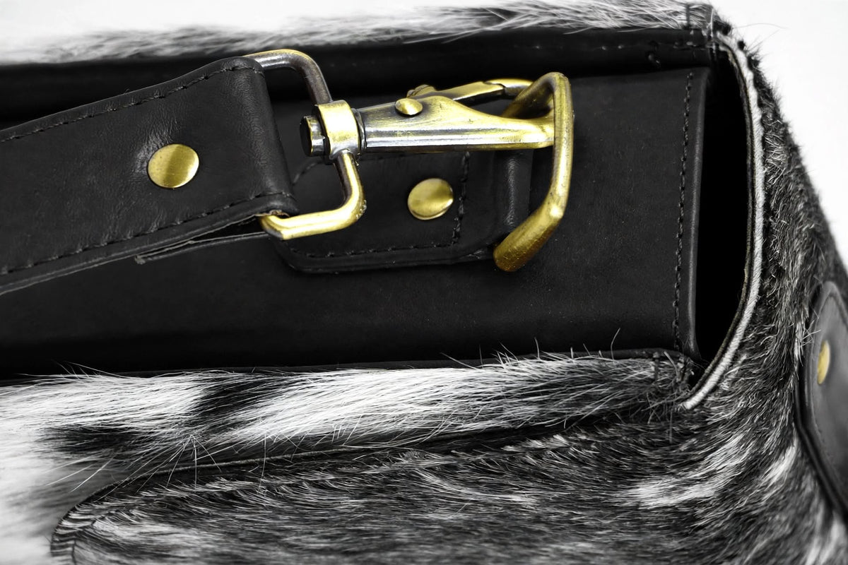 "Close-up detail of brass buckle and [Trim Color] leather strap on spotted cowhide bag