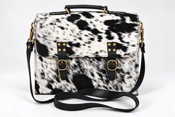 Salt and pepper spotted cowhide messenger bag with black leather trim and brass buckle straps - front view hero shot on white background