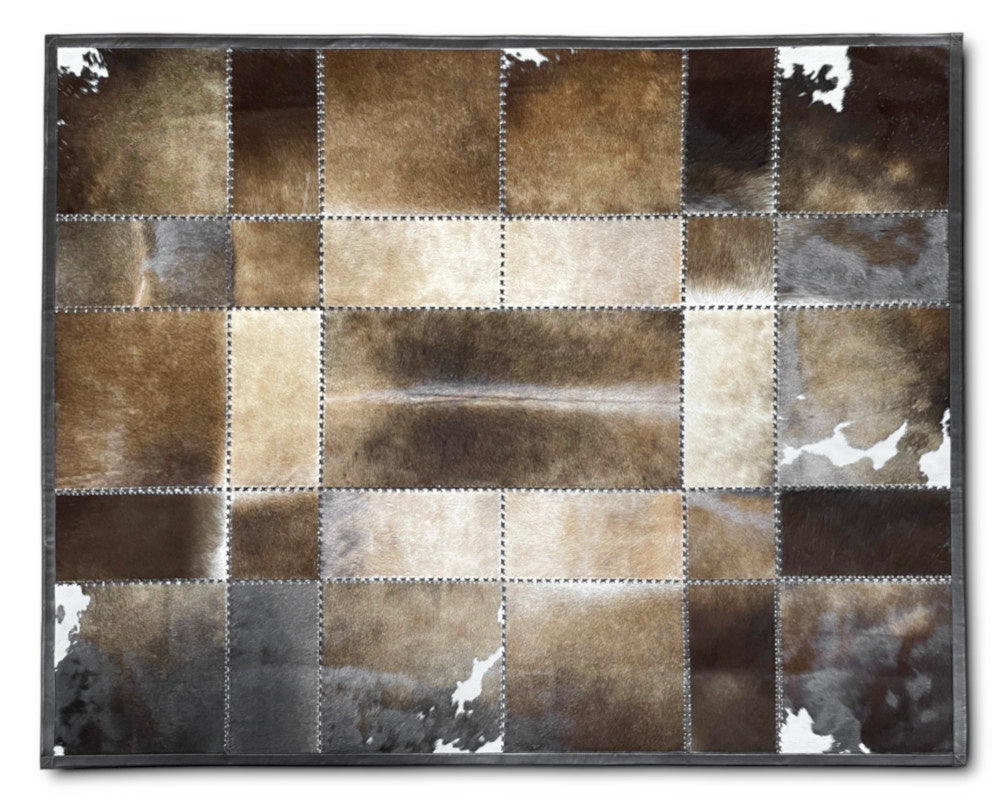 A rectangular patchwork rug made of stitched cowhide or faux-hide panels in mixed brown, beige, gray, and black tones, shown flat against a plain white background.