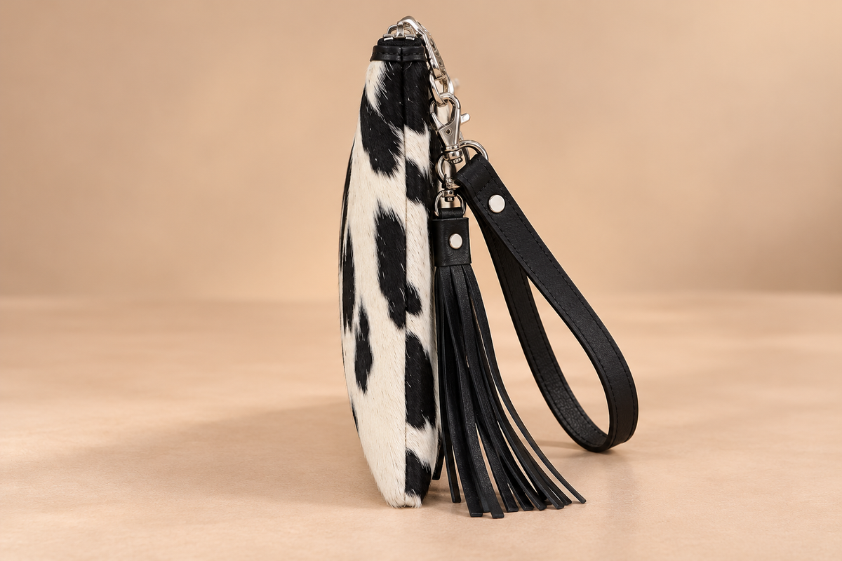 Side profile of black and white cowhide leather wristlet clutch showing bag depth, leather edging, and zipper construction