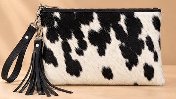 Black and white genuine cowhide wristlet bag with leather trim, zipper closure, detachable wrist strap, and fringe tassel