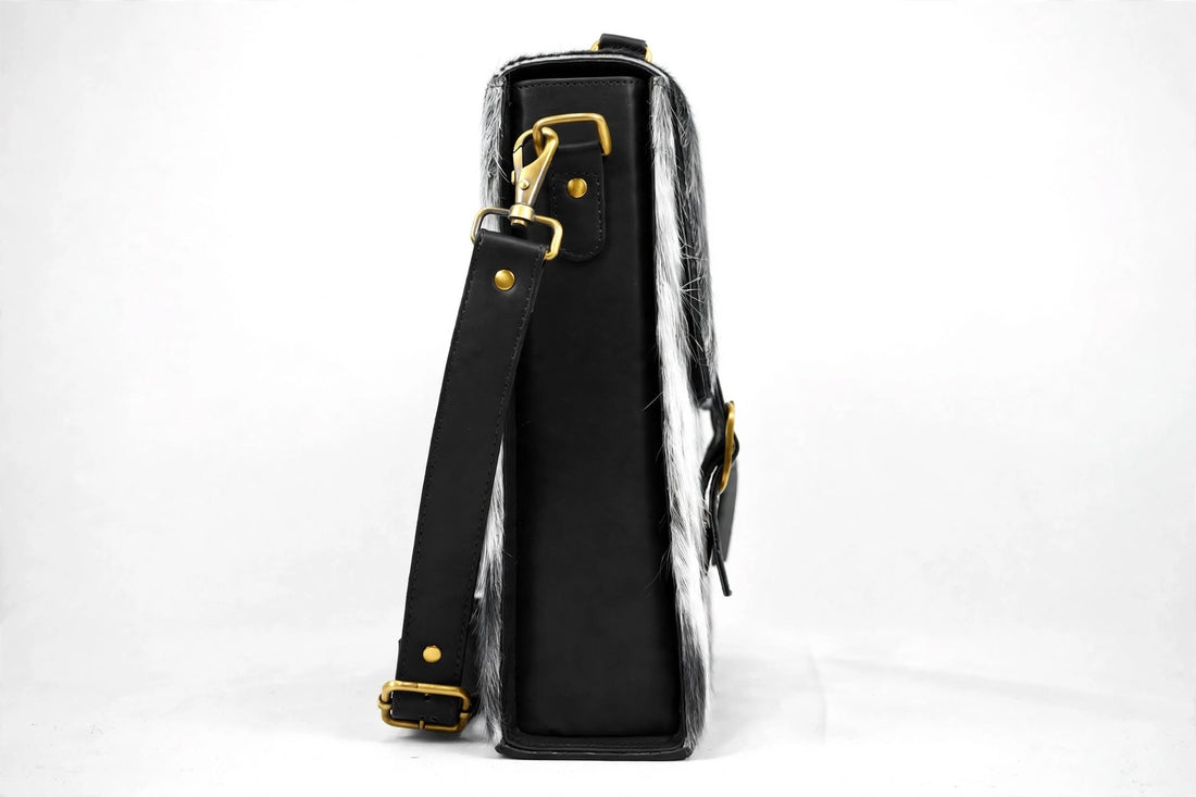 Salt and pepper spotted cowhide messenger bag with black leather trim and brass buckle straps - front view hero shot on white background